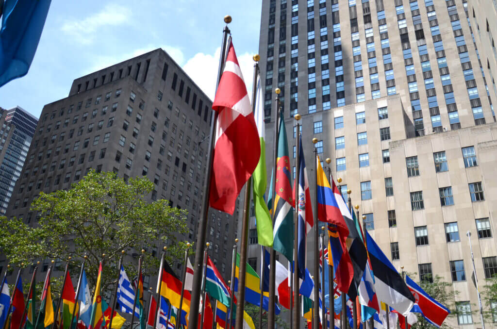 A photo of flags from many different countries at Rockefeller Center in Manhattan, New York. The background shows the Rockefeller building.