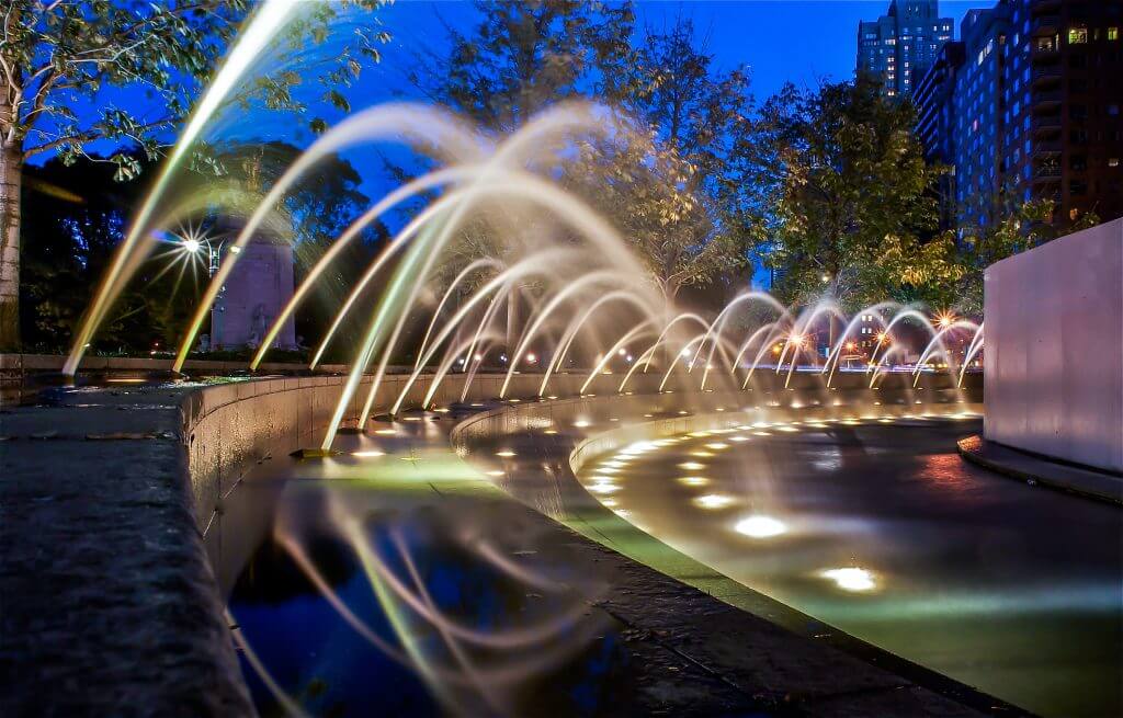 This image shows the Columbus Circle fountains in New York City at night. 