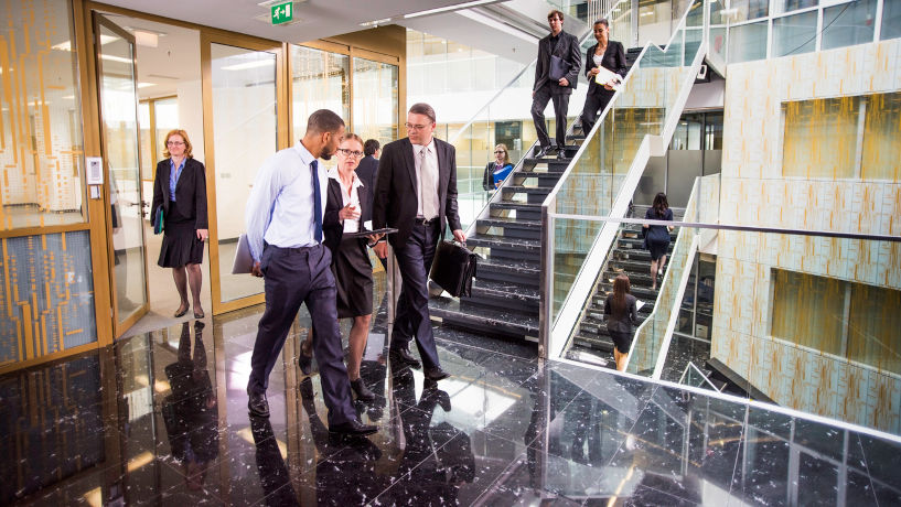 Business people rushing through a glass-walled corridor.