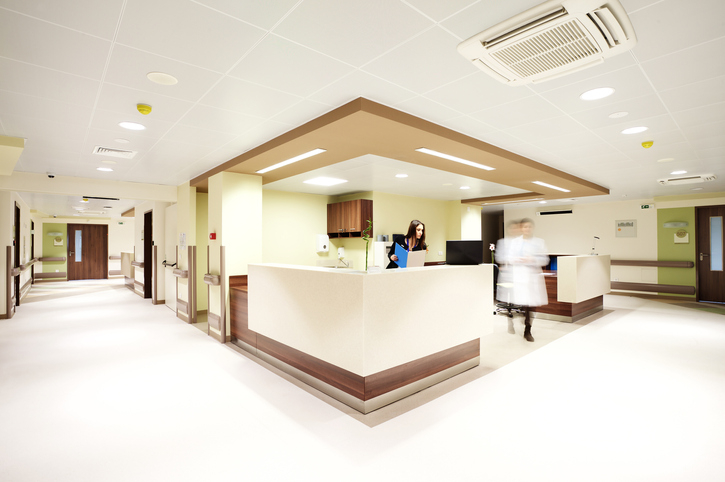Reception in a modern hospital with a receptionist and a blurred doctor figure.